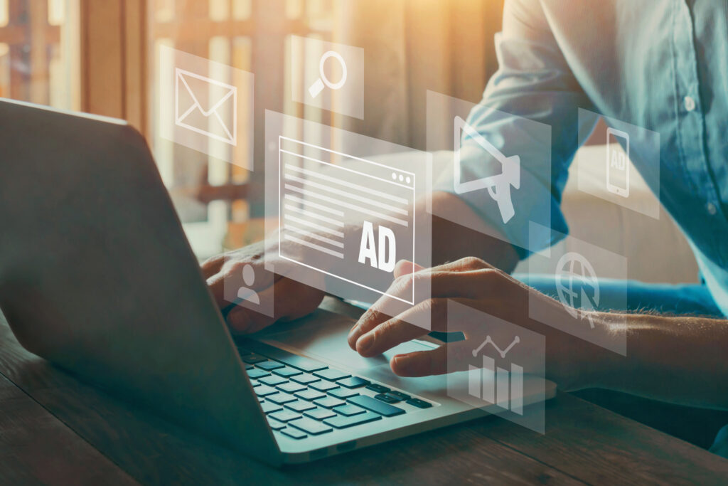 A man typing on a laptop with ad logos coming out of it.